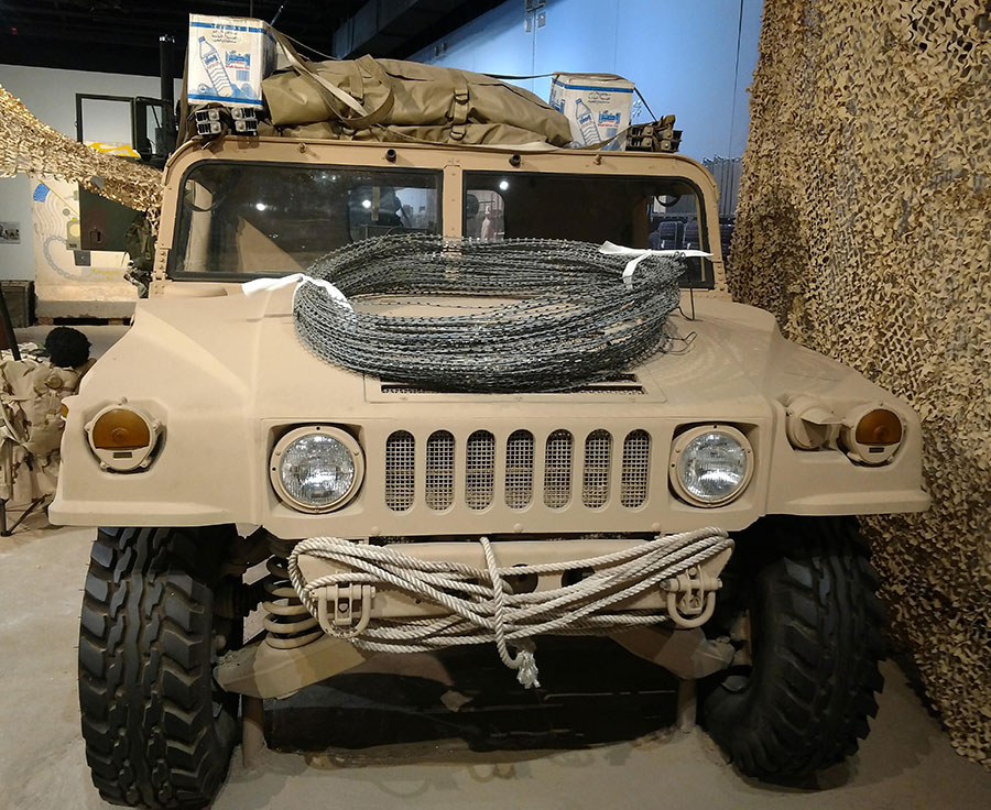 A tan US Army vehicle as part of an exhibit inside the US Army Transportation Museum.